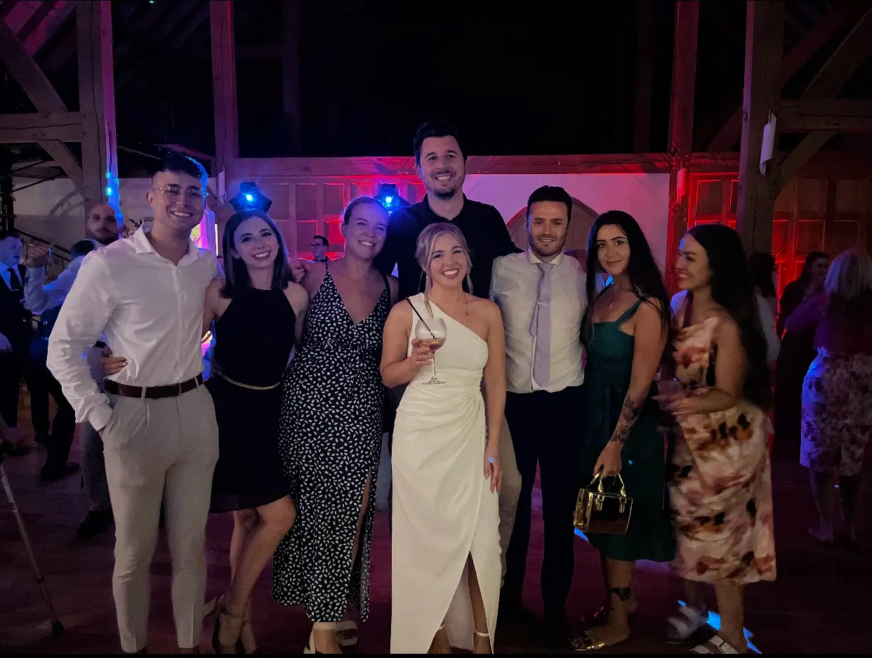 A group of people posing for a photo with a bride in her wedding dress stood in the middle with disco lighting