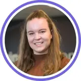 A headshot of a smiling brunette woman with long hair wearing a rusty brown top with a purple ring around the image.