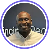 A headshot of a smiling bald man wearing a white shirt with a purple ring around the image.